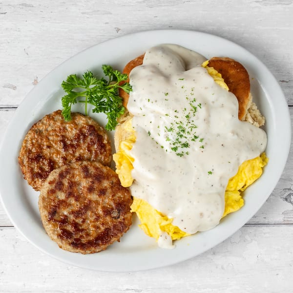 A breakfast platter with two sausage patties, scrambled eggs, biscuits and gravy, garnished with parsley.