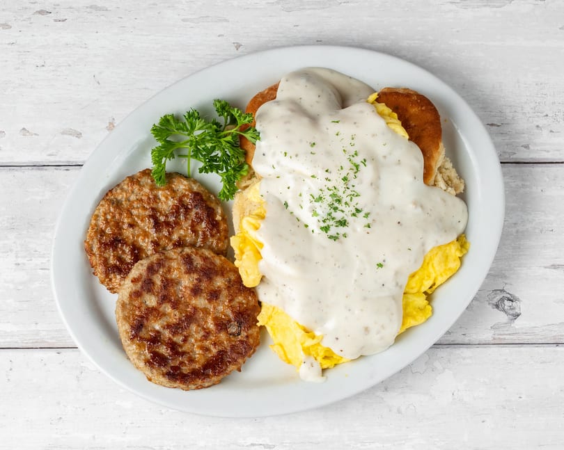A breakfast platter with two sausage patties, scrambled eggs, biscuits and gravy, garnished with parsley.