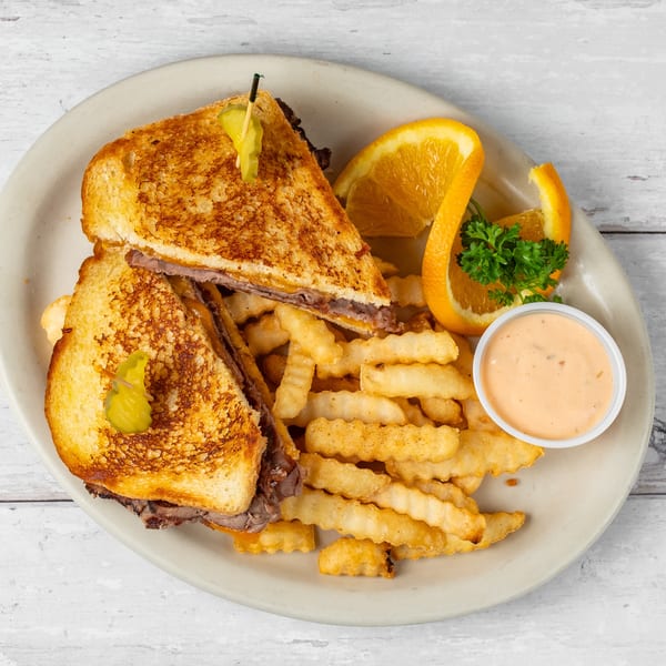 Grilled sandwich with meat and cheese, crinkle-cut fries, orange slices, and dipping sauce on a plate.