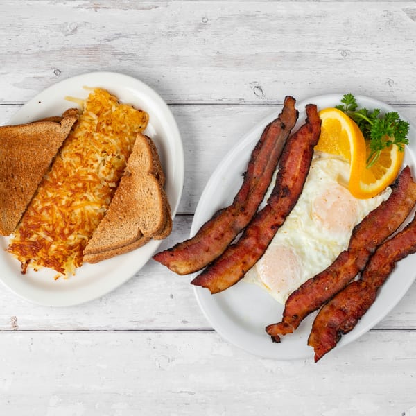Two plates of breakfast food, one with hash browns and toast, the other with bacon and eggs.