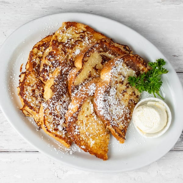 Golden brown French toast slices dusted with powdered sugar, served with butter and parsley on a white plate.
